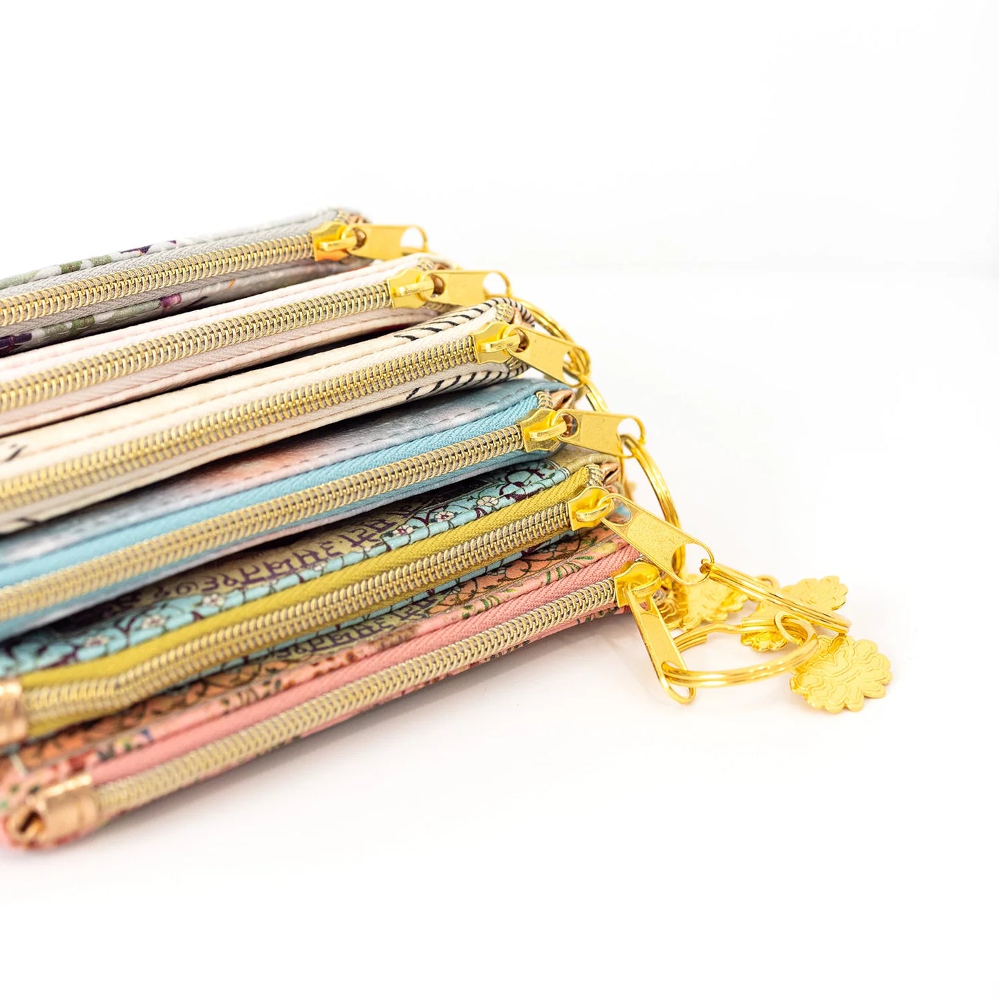 Stack of colorful zipped pouches with a gold keychain on a white background