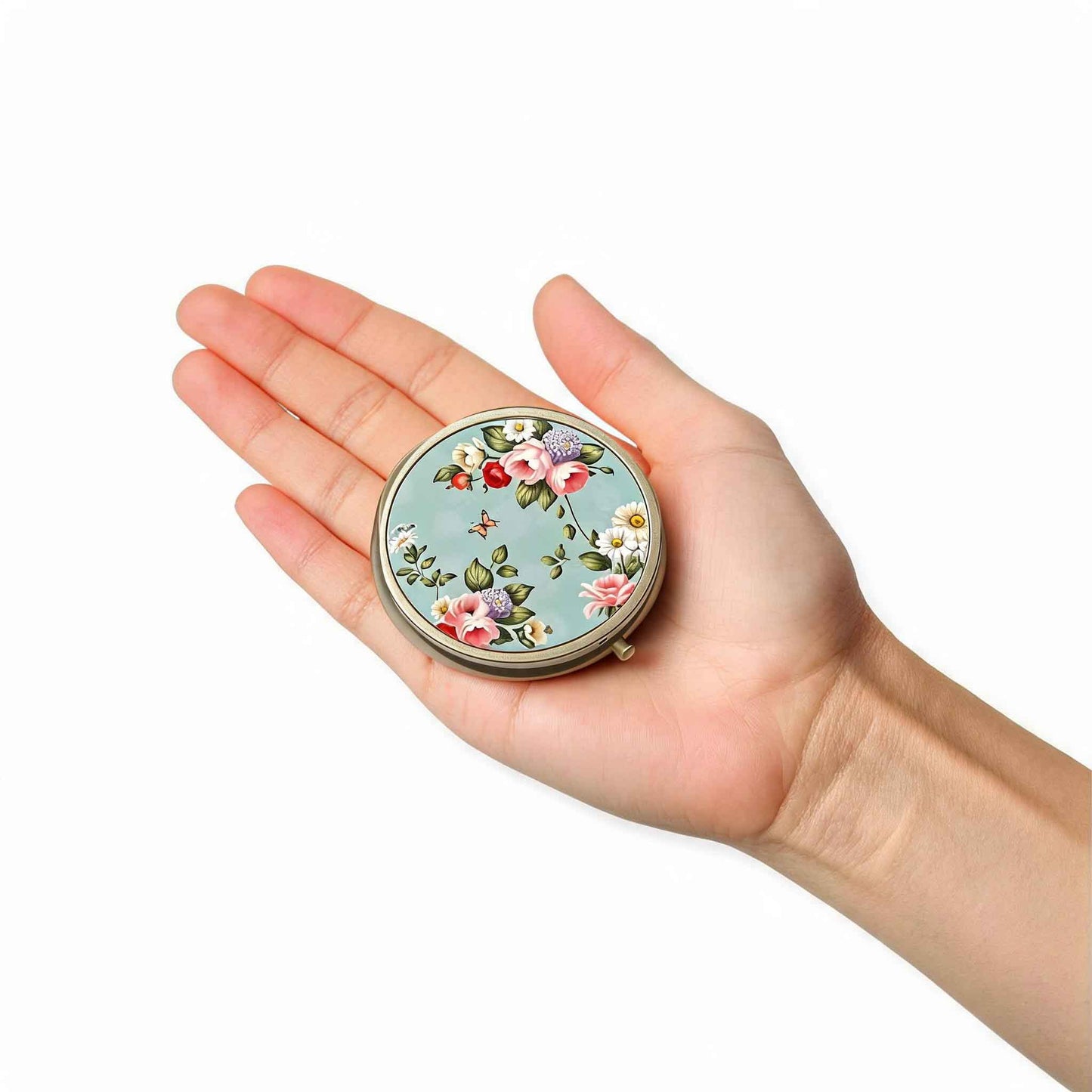 Round light blue floral pillbox shown in hand to demonstrate compact travel size