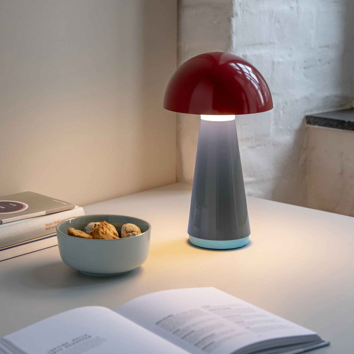 Mushroom-shaped lamp on a table with an open book and bowl of snacks.