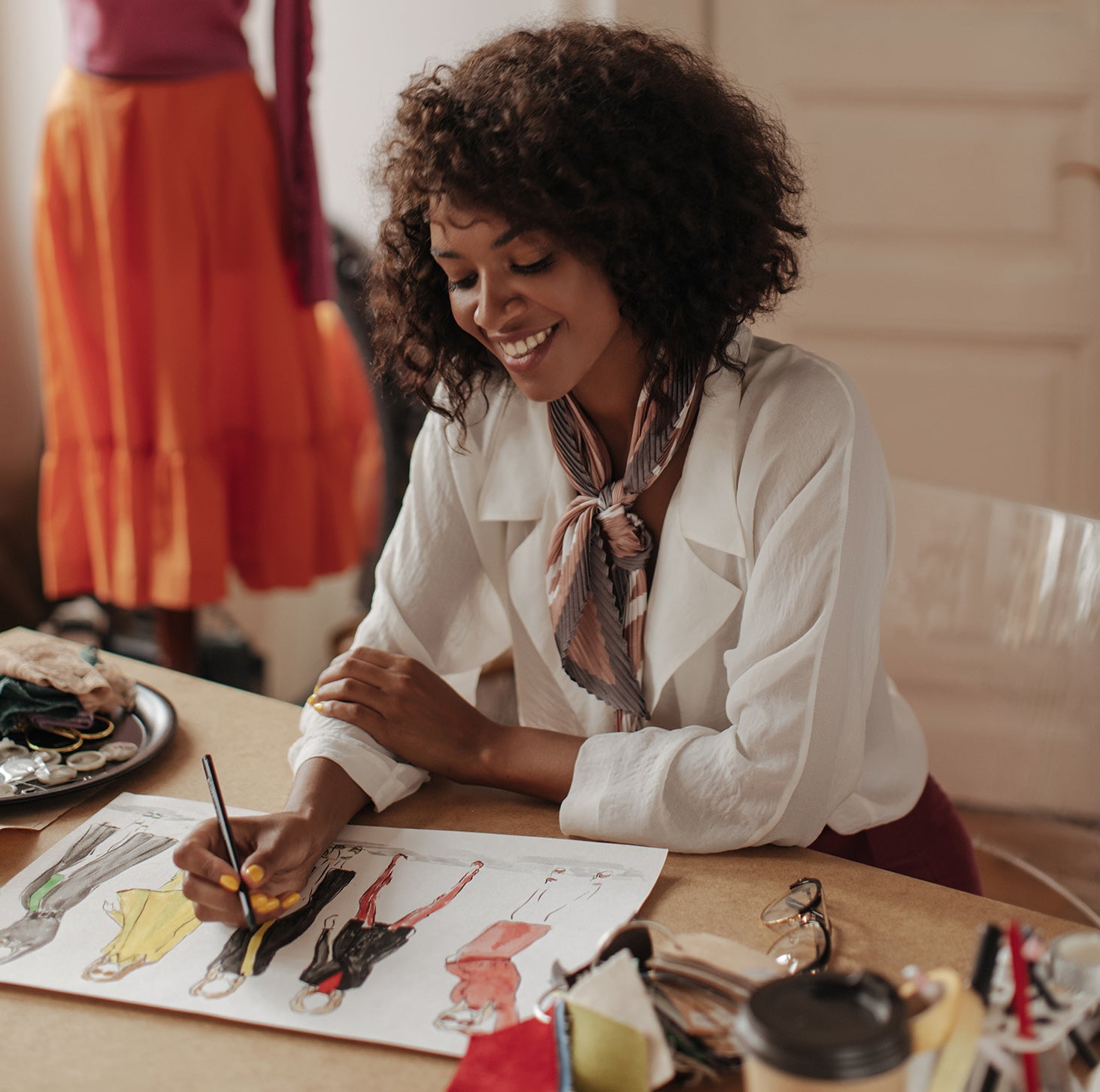 Fashion designer sketching colorful clothing designs at a creative studio desk with fabric swatches and accessories