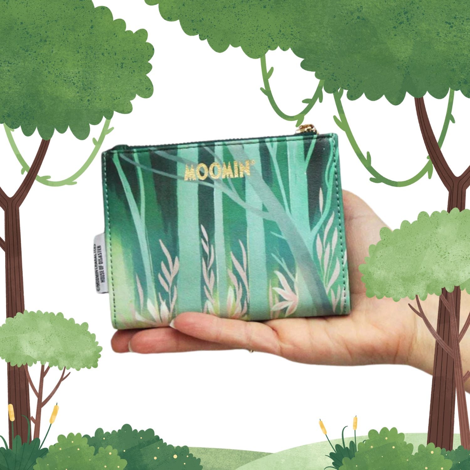 Hand holding a green wallet with 'Moomin' branding against a cartoon forest background