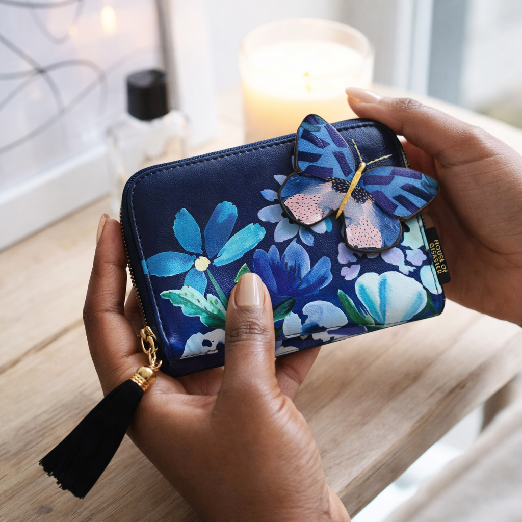 Navy blue floral wallet with a butterfly charm held by a hand on a wooden surface.