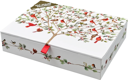 A white rectangular gift box with a lid printed with a winter tree of life design featuring red cardinals, green pine branches, and small birds. A red ribbon tie is visible at the center front, and a small tag at the top reads 'SELF-ADHESIVE ENVELOPE!'.