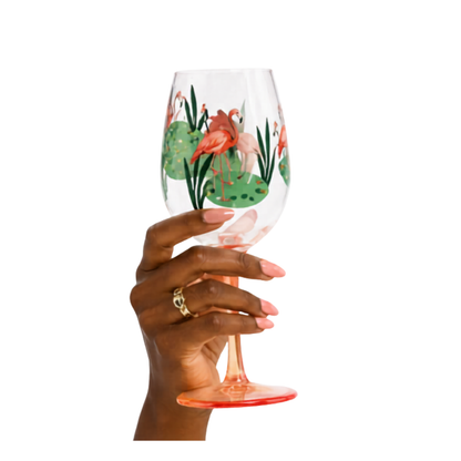 Hand holding an acrylic wine glass with flamingo and lily pad design on a white background