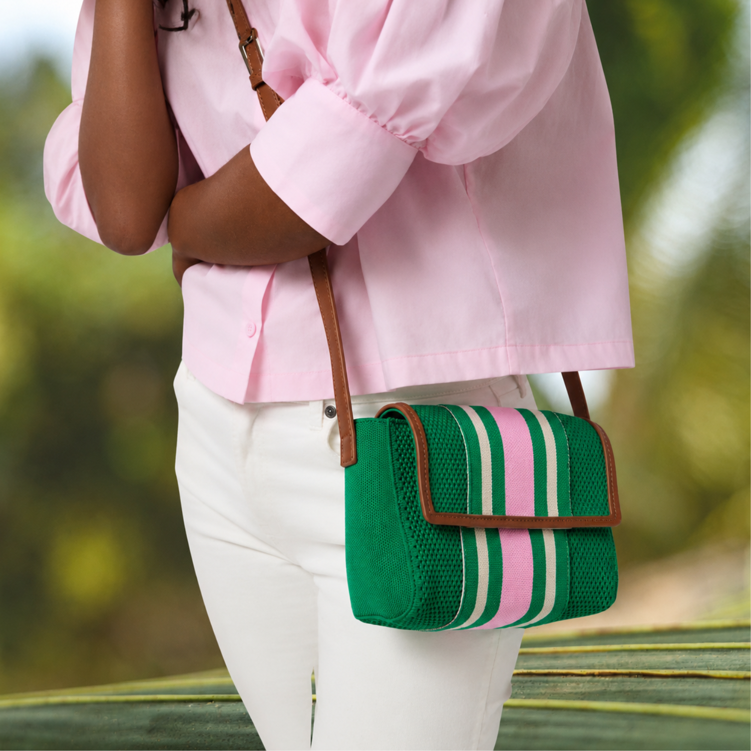 Woman wearing a pink jacket with a green and pink striped bag on a blurred natural background