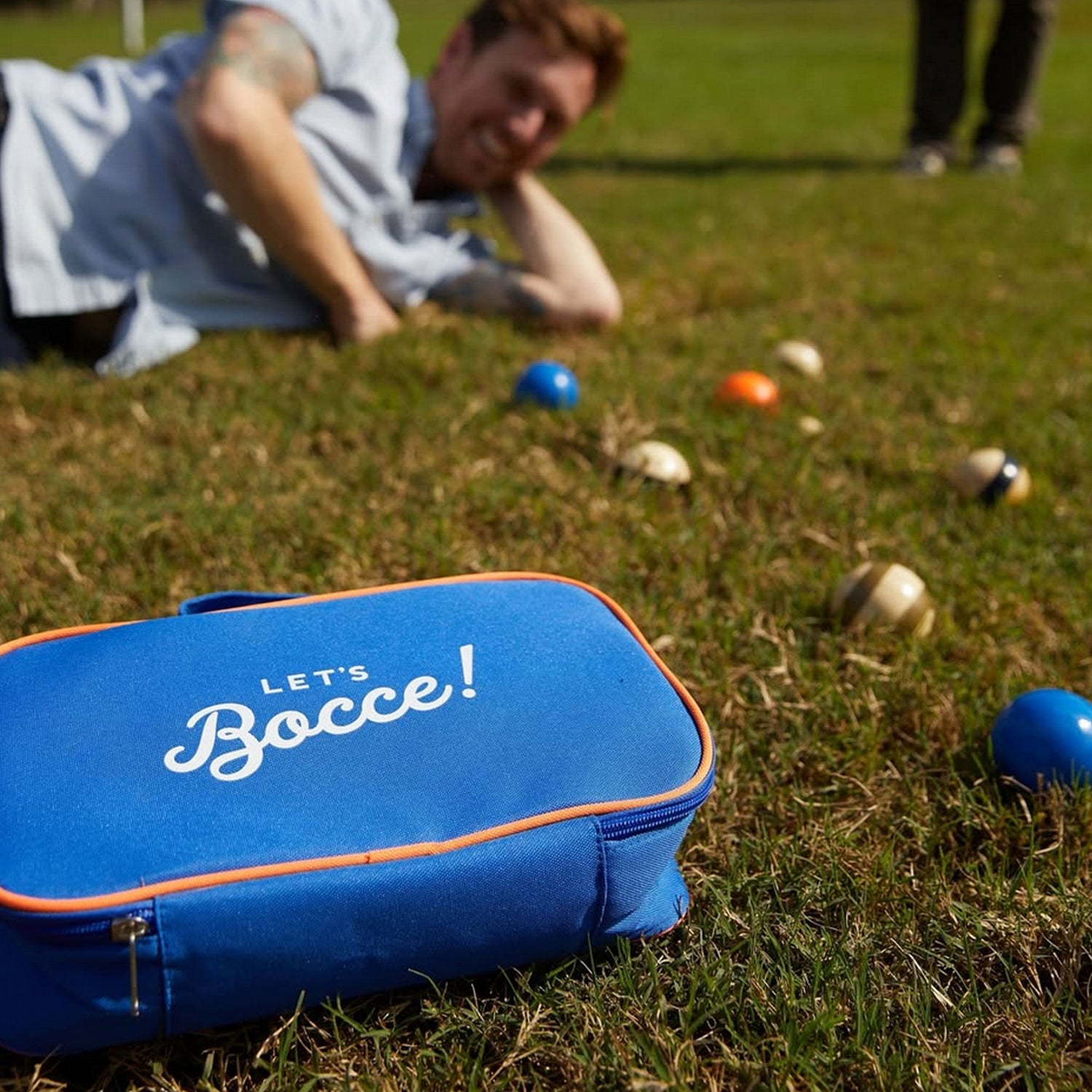 Blue 'Let's Bocce!' bag on grass with bocce balls scattered around
