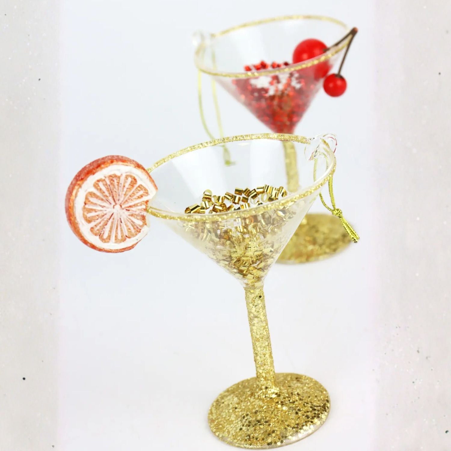 Gold glittery cocktail glass Christmas ornaments with a slice of  orange and cherry on a white background