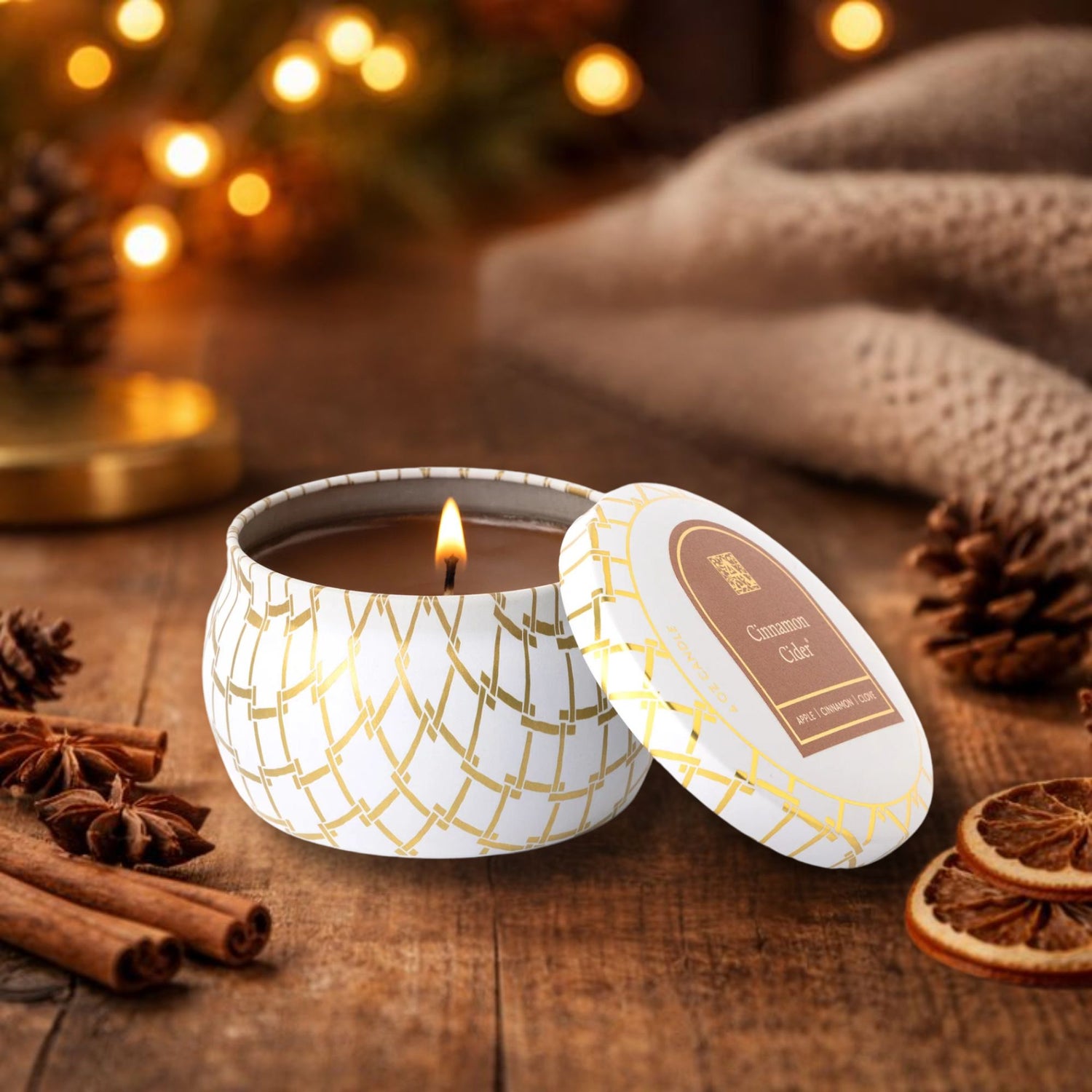 Cinnamon cider candle in a decorative tin with cinnamon sticks and pine cones on a wooden surface.