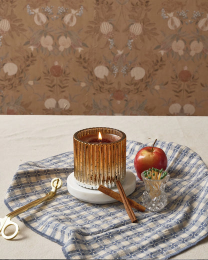 Cinnamon spice candle on a decorative plate with an apple and cinnamon stick, against a floral wallpaper background.