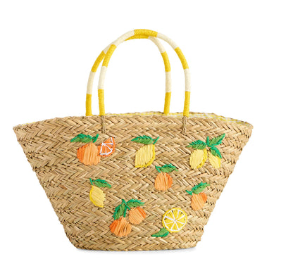 A natural woven straw tote bag decorated with embroidered pineapples, lemons, and orange slices, featuring dual handles with yellow and white stripes, set against a plain white background.