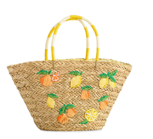 A natural woven straw tote bag decorated with embroidered pineapples, lemons, and orange slices, featuring dual handles with yellow and white stripes, set against a plain white background.