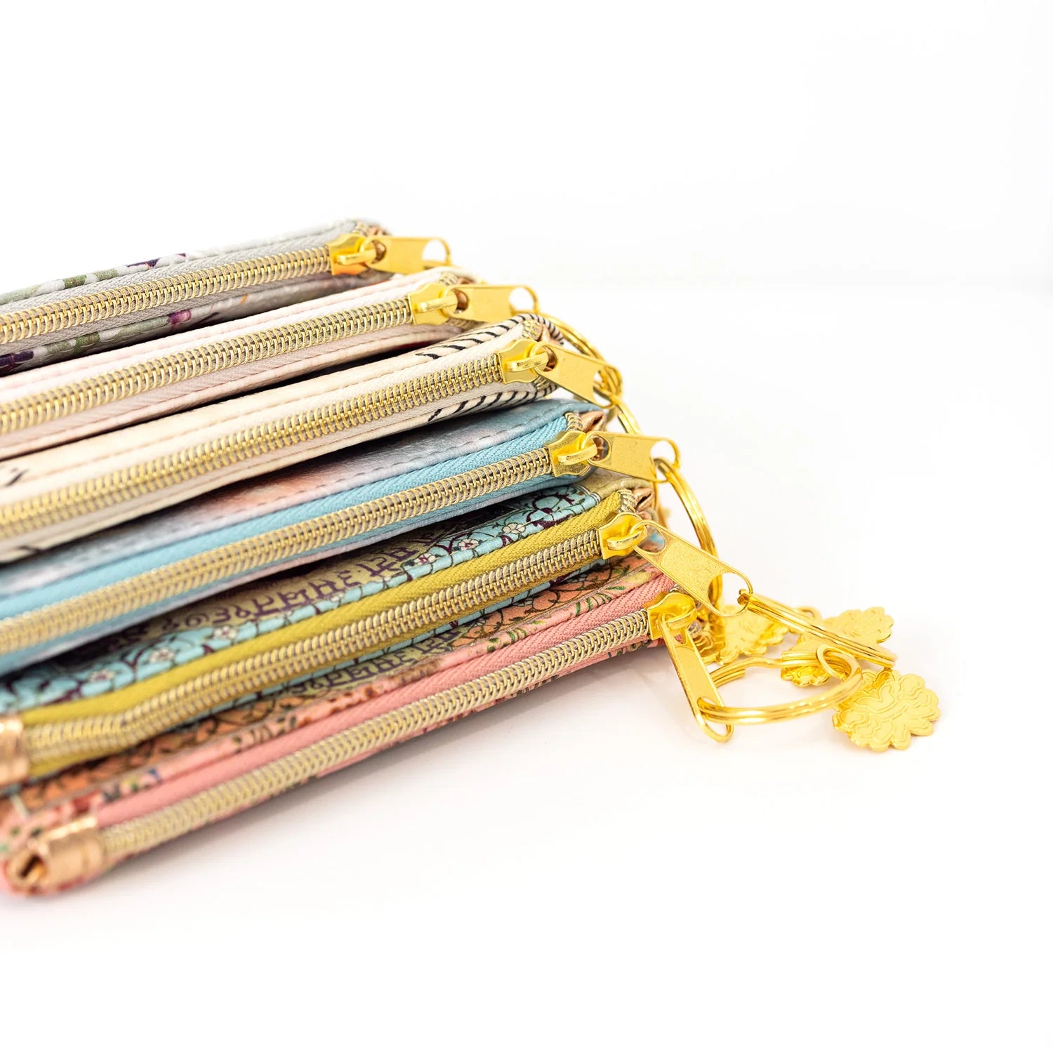 Stack of colorful zipped pouches with a gold keychain on a white background