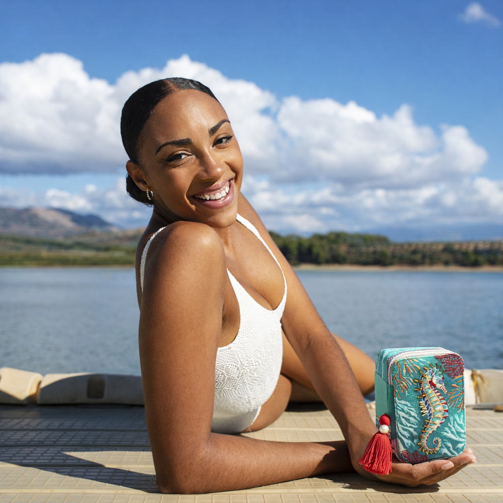 Woman in a white swimsuit holding a colorful pouch by a lake with mountains in the background