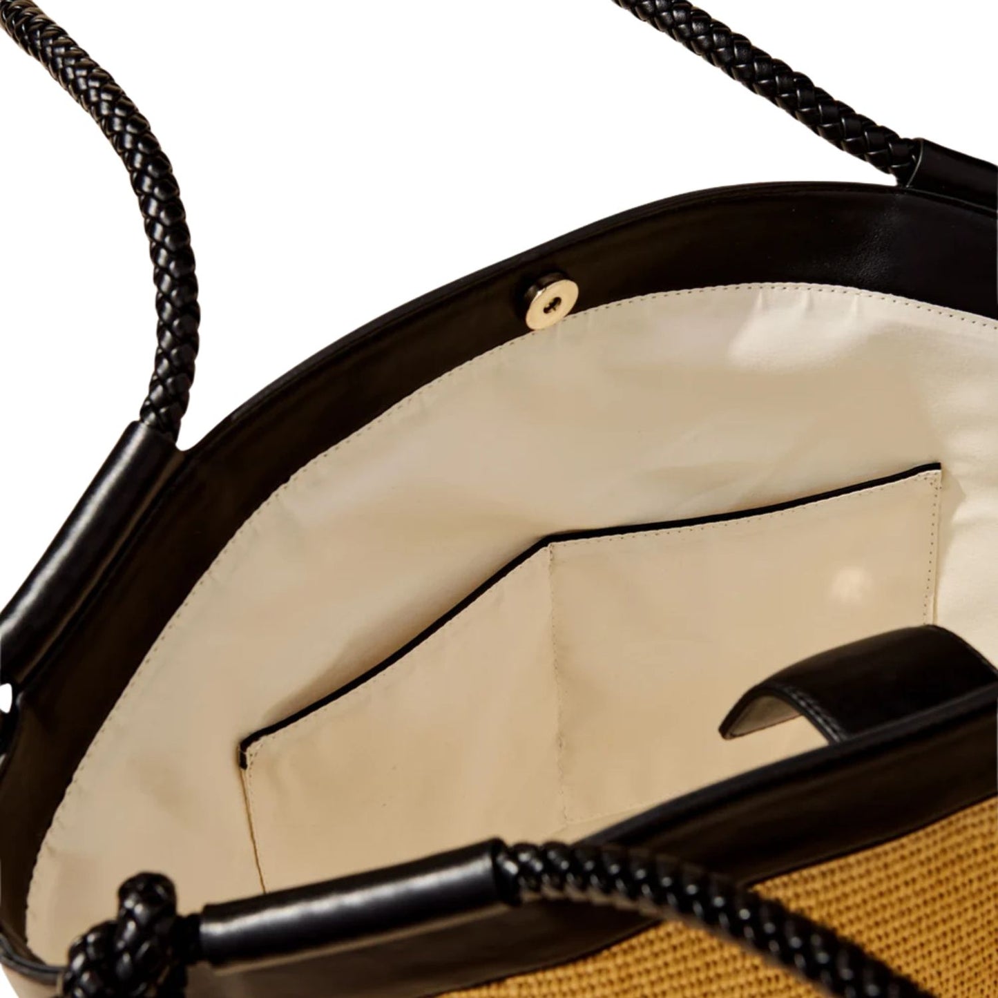 Close-up of the interior of a woven straw tote bag with black leather trim, black braided shoulder straps, and a cream-colored fabric lining.