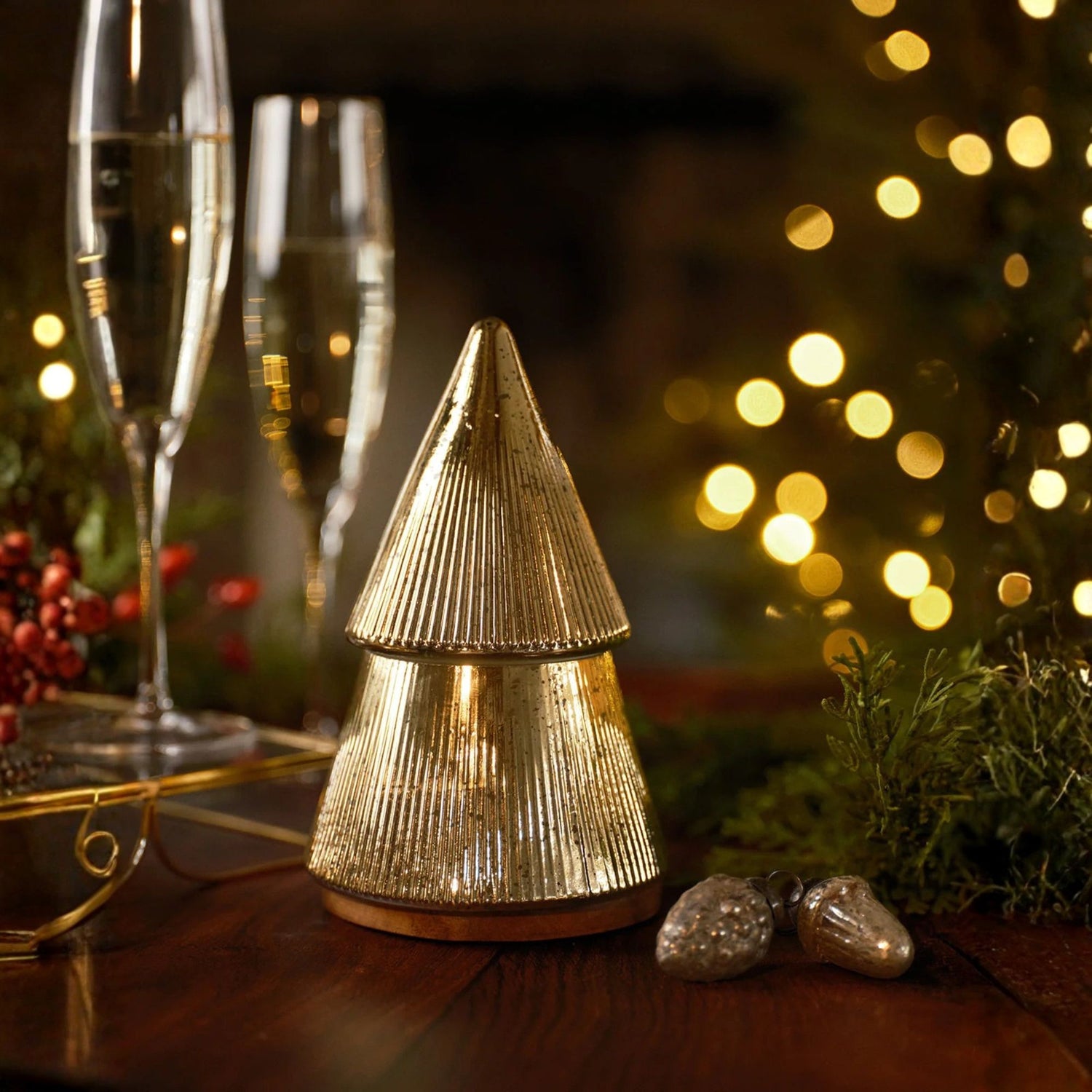 Decorative gold tree-shaped candle holder on a table with blurred lights in the background