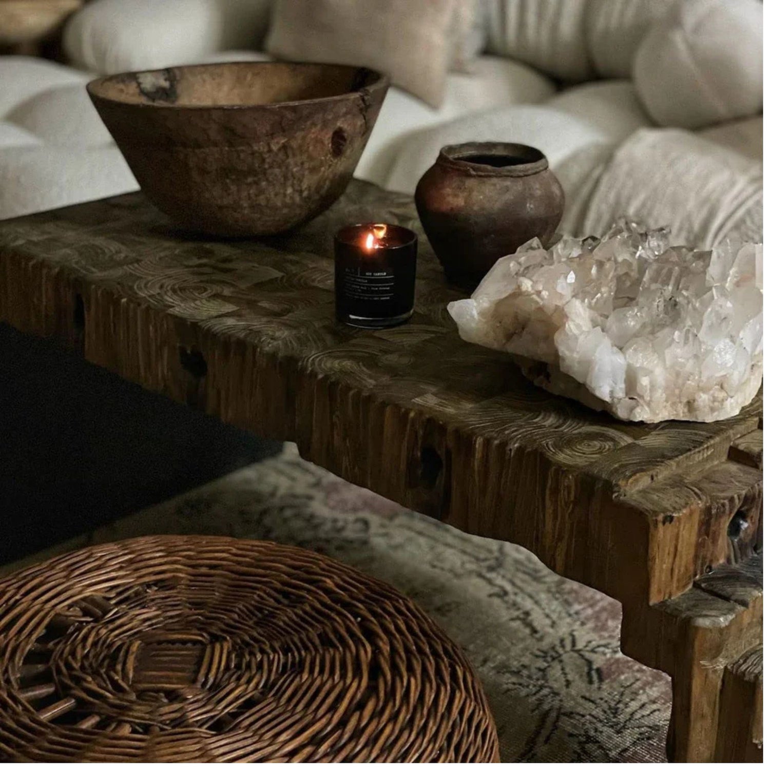 Decorative setting with rustic bowls, a lit candle, and crystals on a wooden surface.