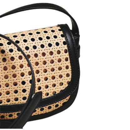 Close-up of a woven cane shoulder bag with black leather trim and strap on a white background.