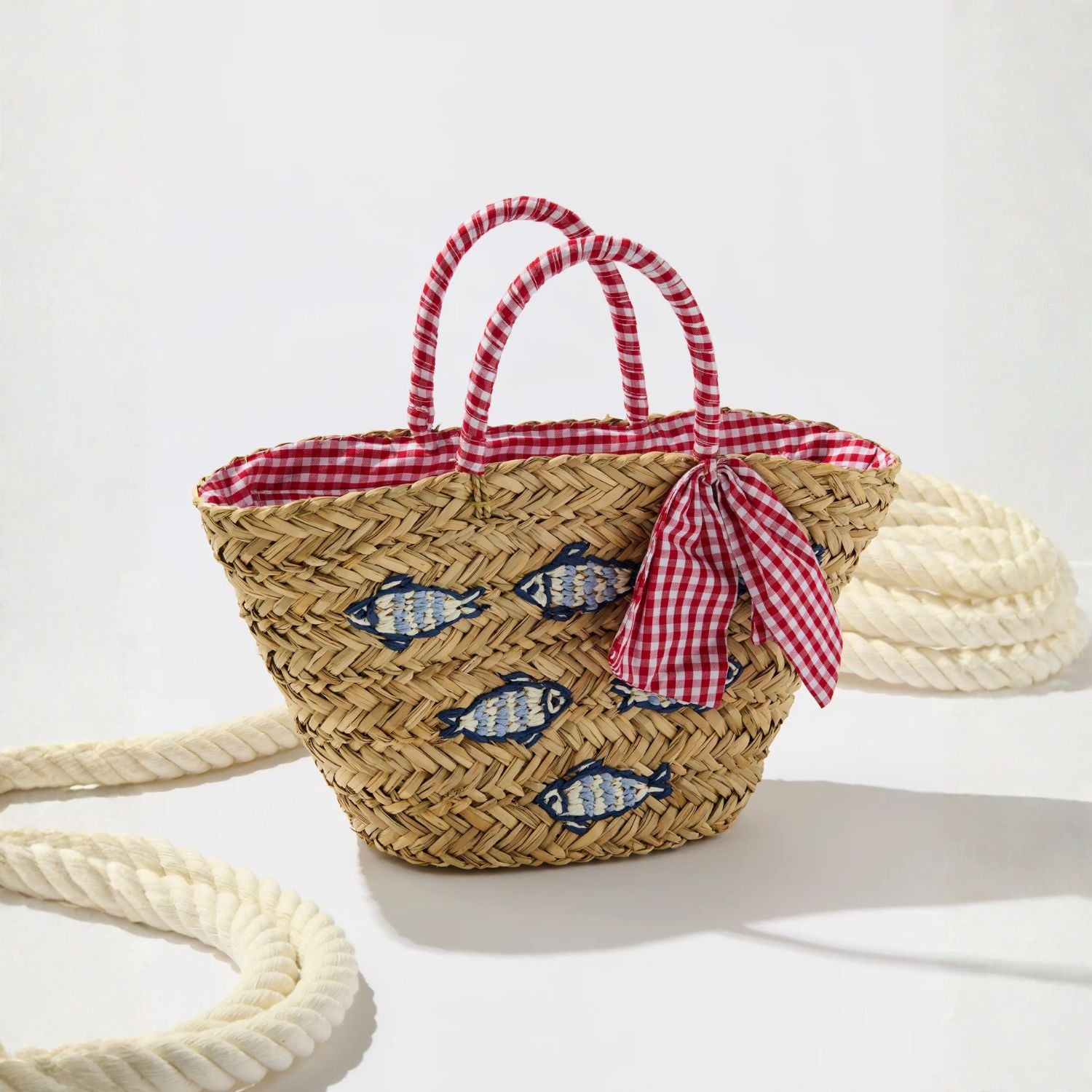Woven basket with fish design and red checkered ribbon on a white background