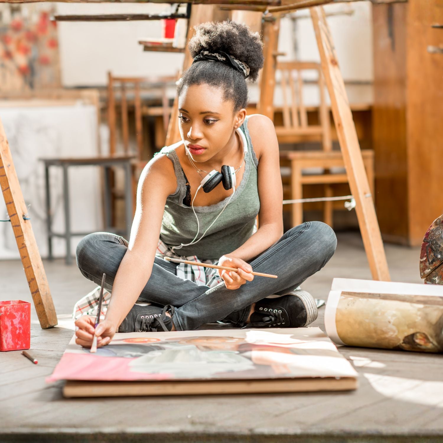 Young artist sitting on the floor painting a large canvas in an art studio.