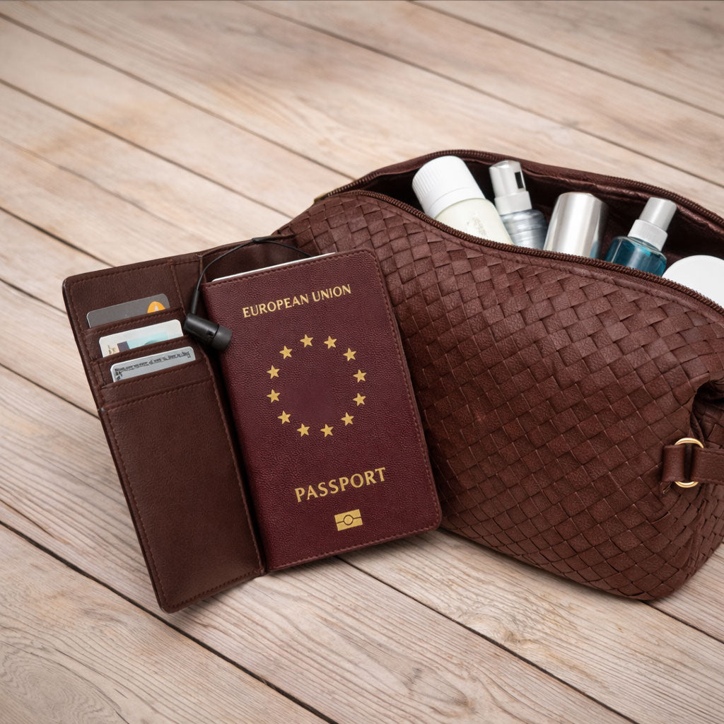 Brown woven travel pouch with toiletries, passport, and wallet on a wooden surface