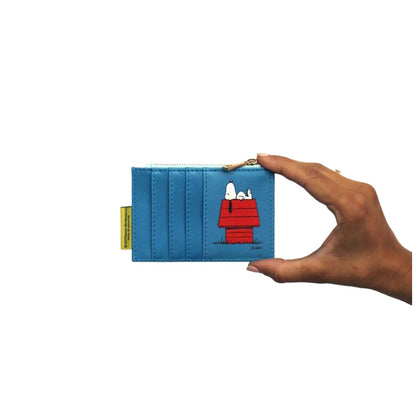 A blue card holder wallet featuring a cartoon print of Snoopy and Woodstock on a red dog house, held by a hand against a white background.