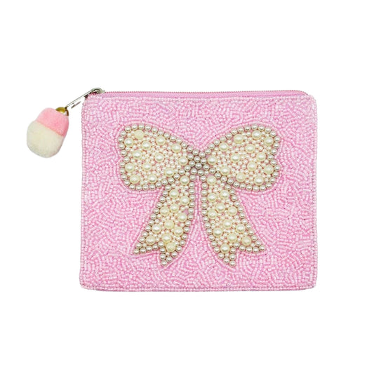 A pink zippered pouch with a textured beaded background and a large bow embellished with pearls and rhinestones. A small pink and white pom-pom charm hangs from the zipper.