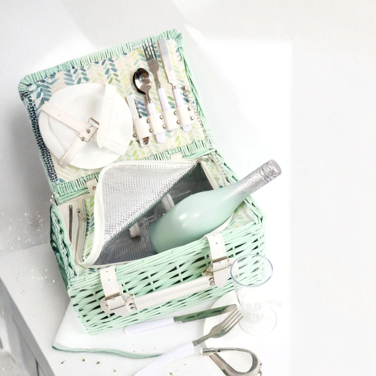 Picnic basket with cutlery, wine bottle, and plates on a white background