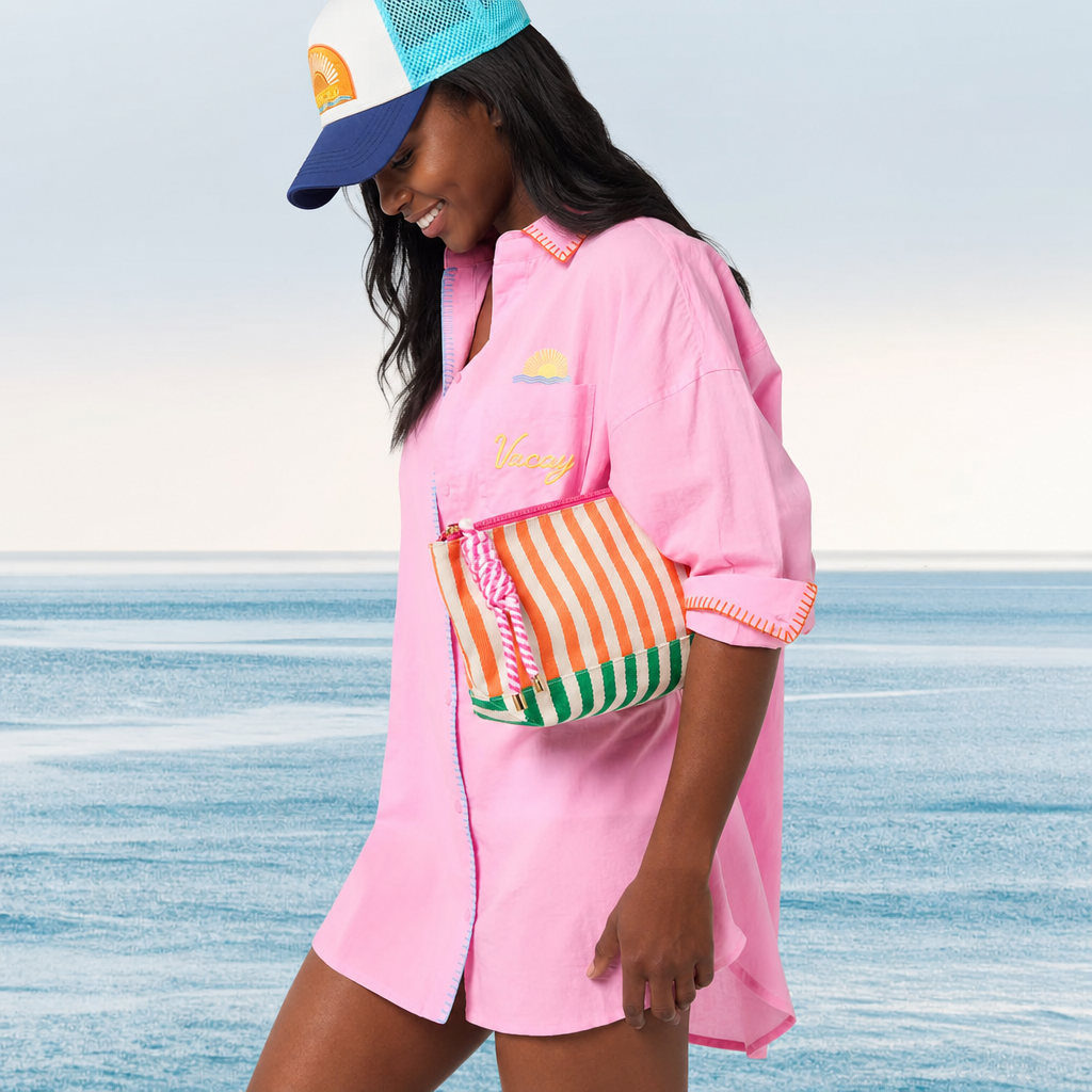 Woman in pink outfit with colorful bag and cap by the ocean