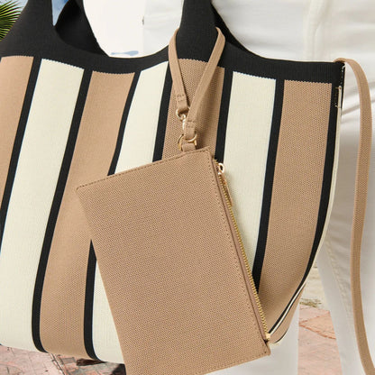 A striped tote bag in beige, cream, and black with a matching zip-around pouch, shown on a mannequin or model in a bright indoor setting.