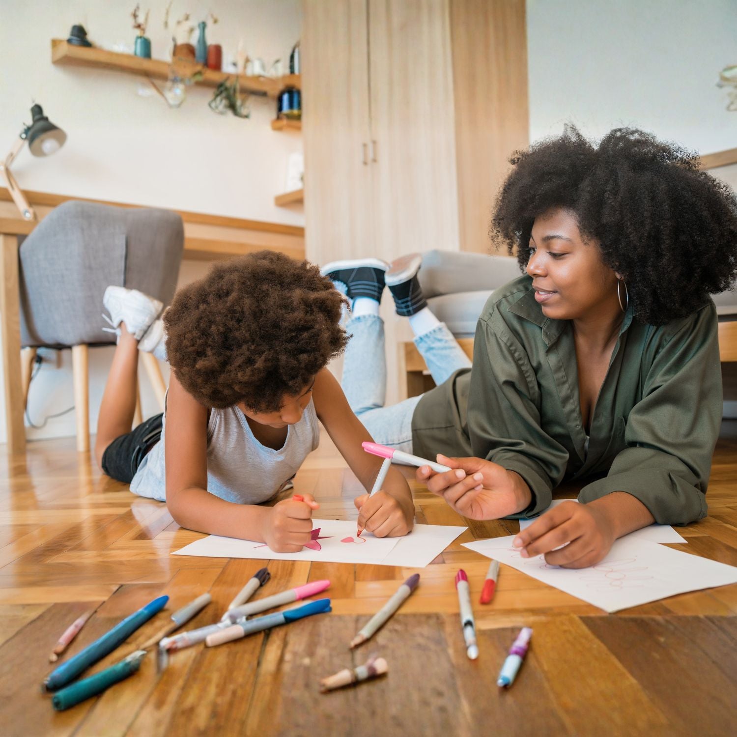 Woman and child lying on the floor with markers, engaged in an activity.