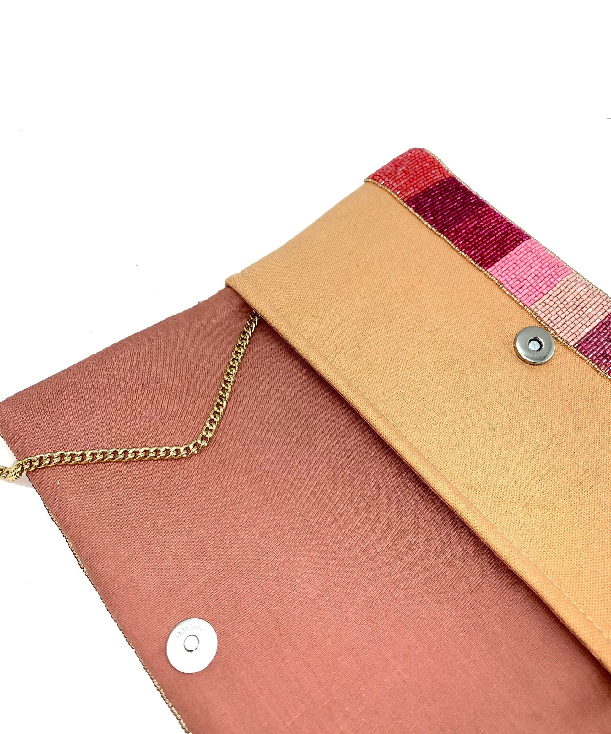 Close-up of a clutch bag with a gold chain, beige top, and pink and red woven detail on a white background
