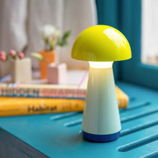 Mushroom-shaped lamp on a blue surface with books and plants in the background