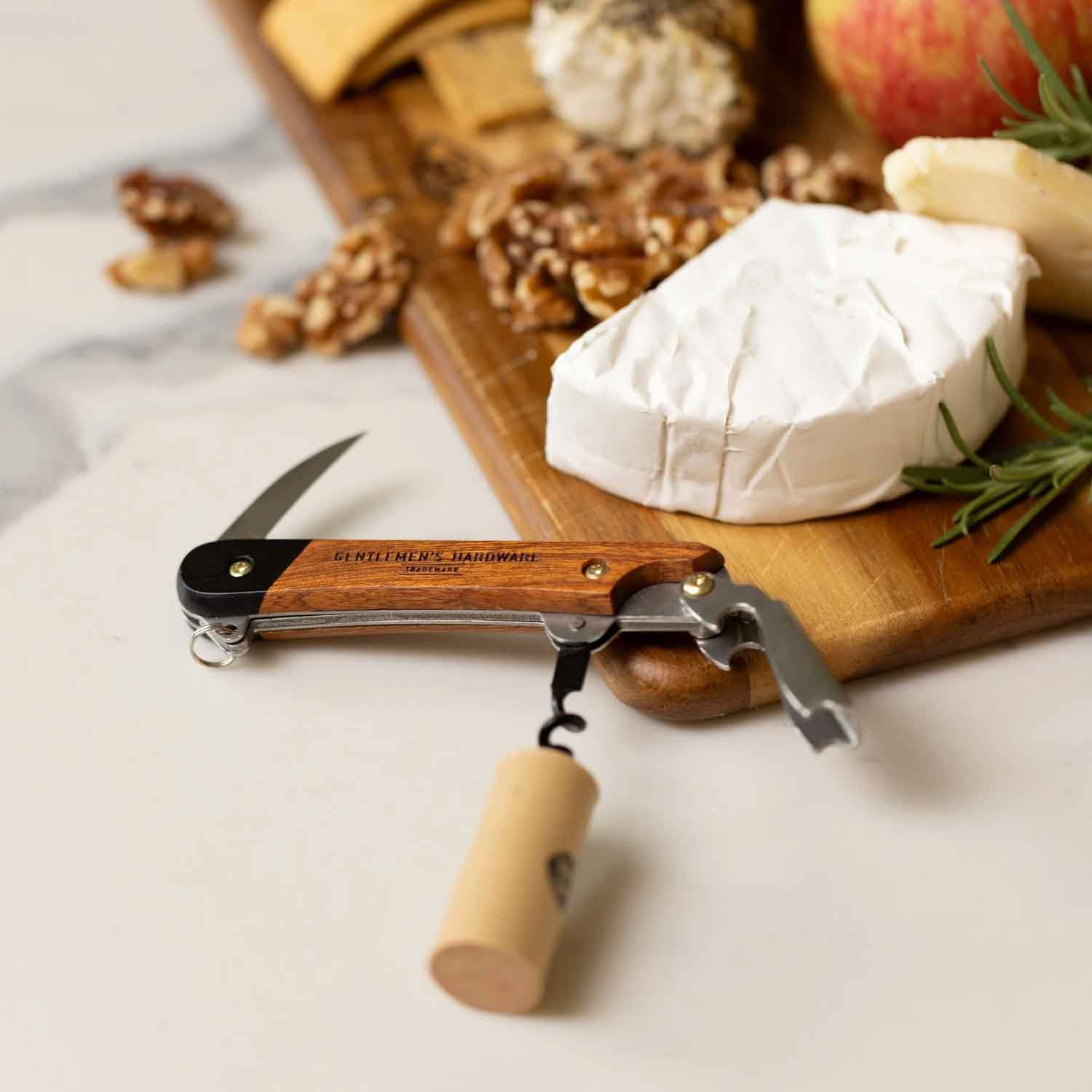 Wooden wine opener knife with corkscrew on a cutting board with cheese and nuts.