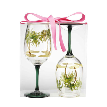 Two acrylic wine glasses with palm tree designs in a box with a pink ribbon
